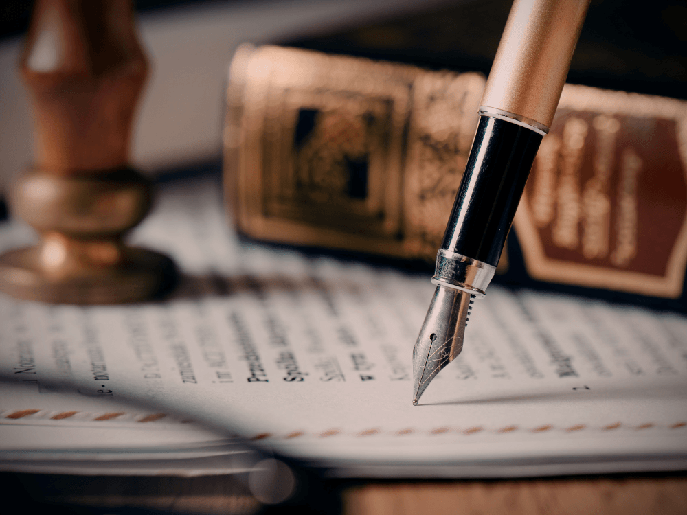Caneta sobre documento jurídico ao lado de livros e carimbo, para explicar quem tem direito ao desconto no registro do primeiro imóvel.