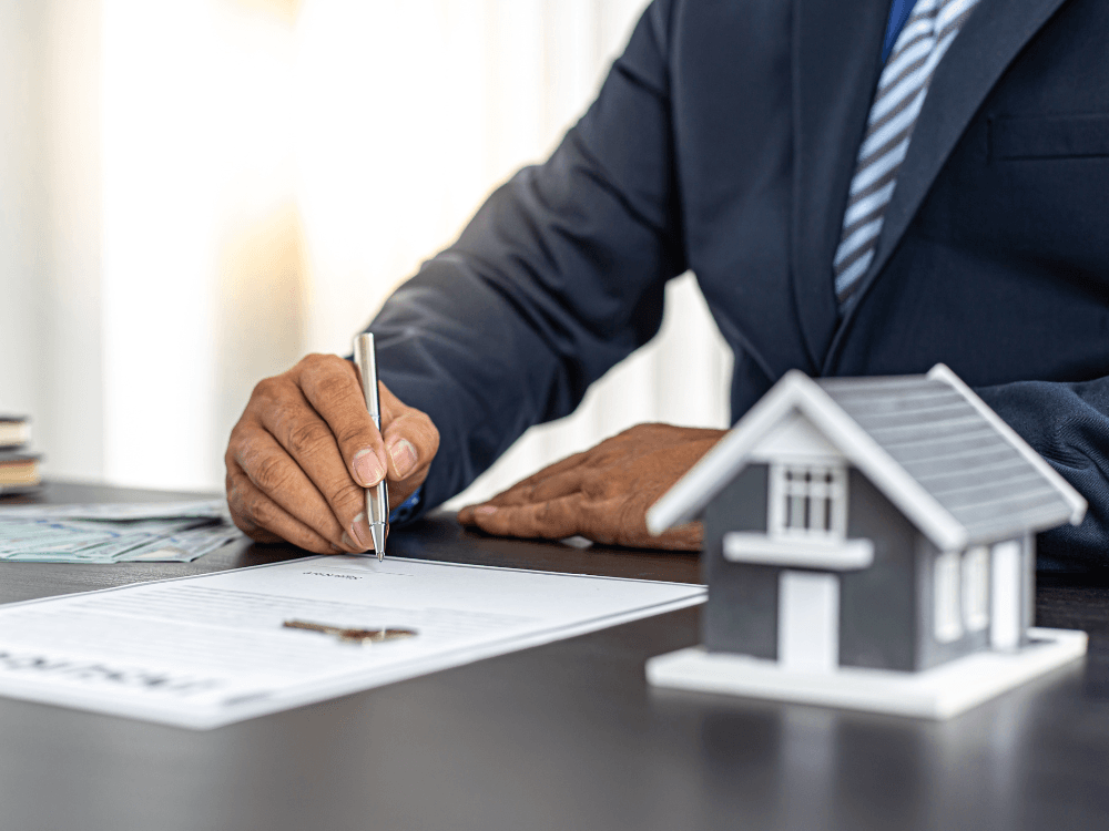 Profissional assina contrato de venda ao lado de uma miniatura de casa, simbolizando a definição da comissão pela intermediação imobiliária.
