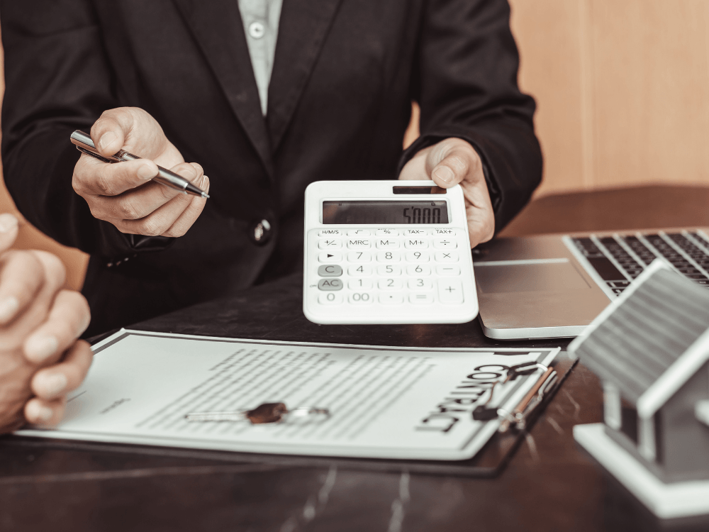 Profissional usa calculadora sobre contrato imobiliário, ilustrando a apuração financeira do ganho de capital na venda de uma propriedade.