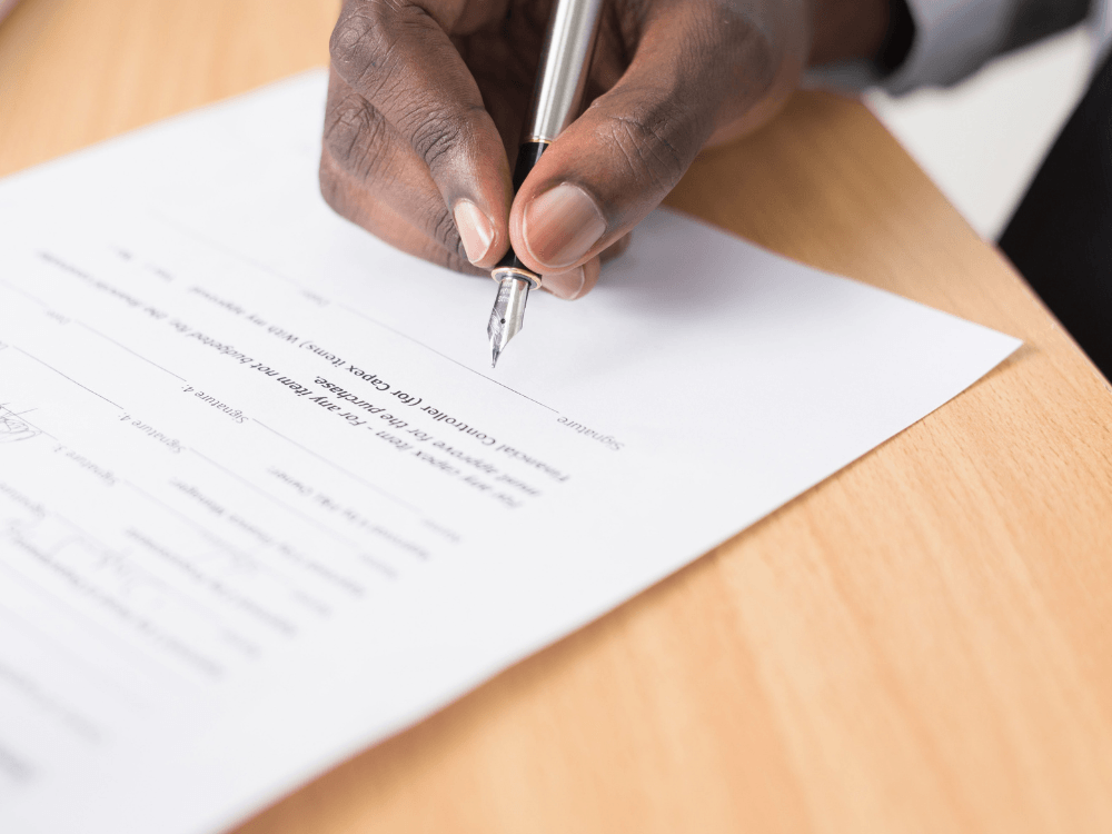 Mão assinando um documento sobre a mesa, representando a formalização do contrato de locação e suas regras de reajuste de aluguel. Tudo para explicar o índice de reajuste aluguel